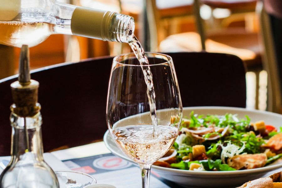 Royce Townhomes White wine is being poured into a glass next to a salad, fresh bread, and condiments on a restaurant table.