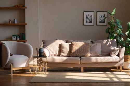 Royce Townhomes Beige sofa with pillows, armchair, side table, plant, and framed art in a sunlit living room with wooden shelves.