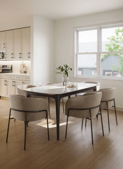 Royce Townhomes Modern dining area with a marble table, six chairs, and sunlight streaming through a window near a kitchen.