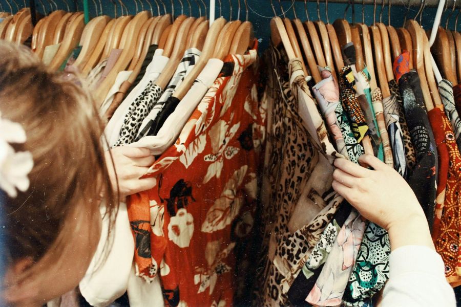 Royce Townhomes A person browses colorful patterned clothes hanging on wooden hangers in a closet or store.