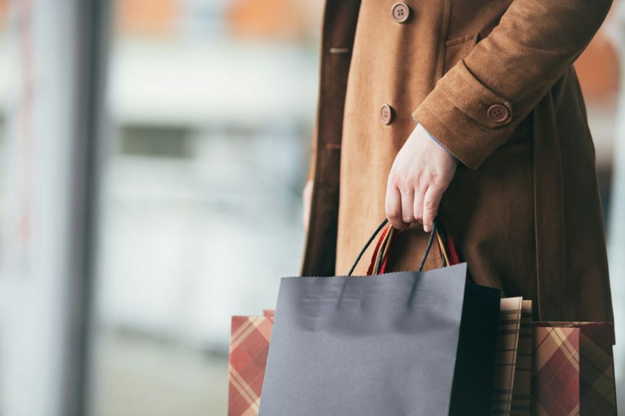 Royce Townhomes A person in a brown coat holds two shopping bags, one black and one plaid, by their handles.
